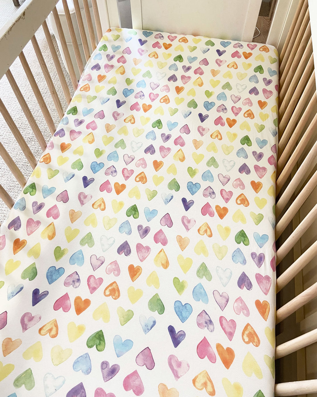 Fitted baby crib sheet in rainbow heart print, designed for a cozy and snug fit on baby or toddler beds